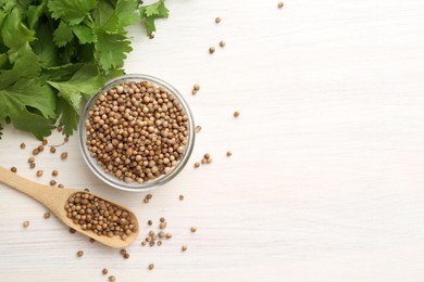 Photo of Coriander seeds in bowl, spoon and fresh cilantro leaves on light wooden table, flat lay. Space for text