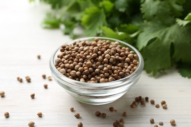 Photo of Coriander seeds in bowl and fresh cilantro leaves on light wooden table, closeup