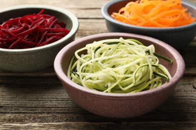 Photo of Different vegetable noodles in bowls on wooden table, closeup. Vegetarian dish