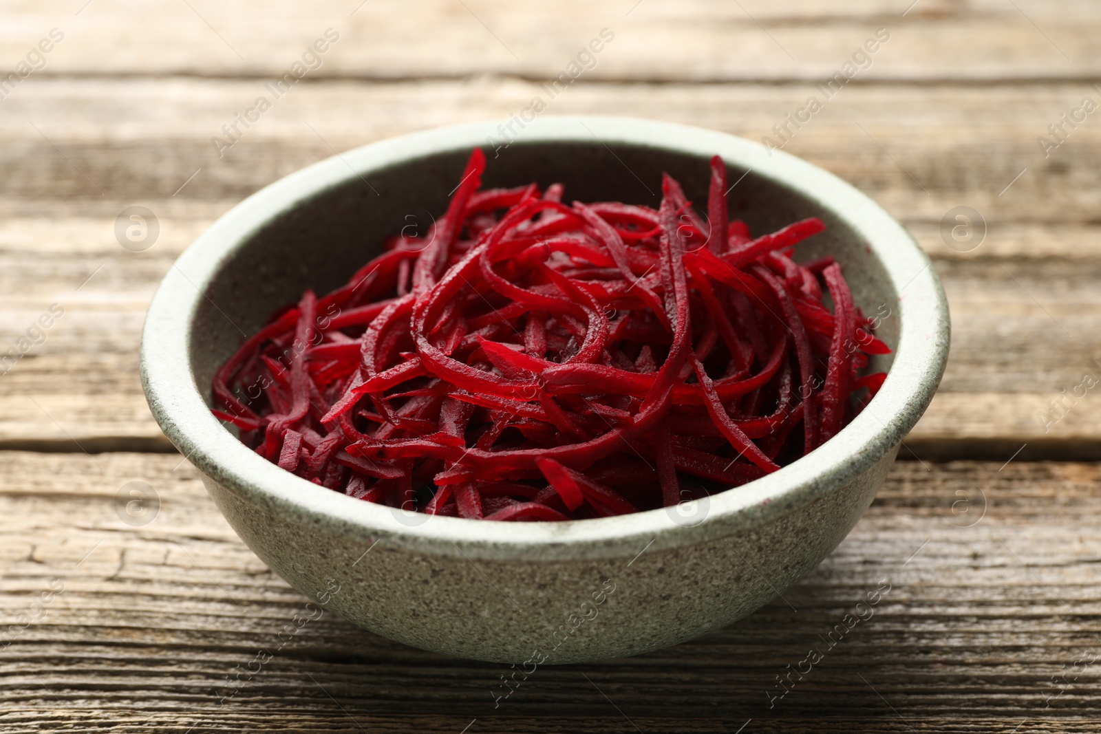 Photo of Raw beetroot noodles in bowl on wooden table, closeup. Vegetarian dish