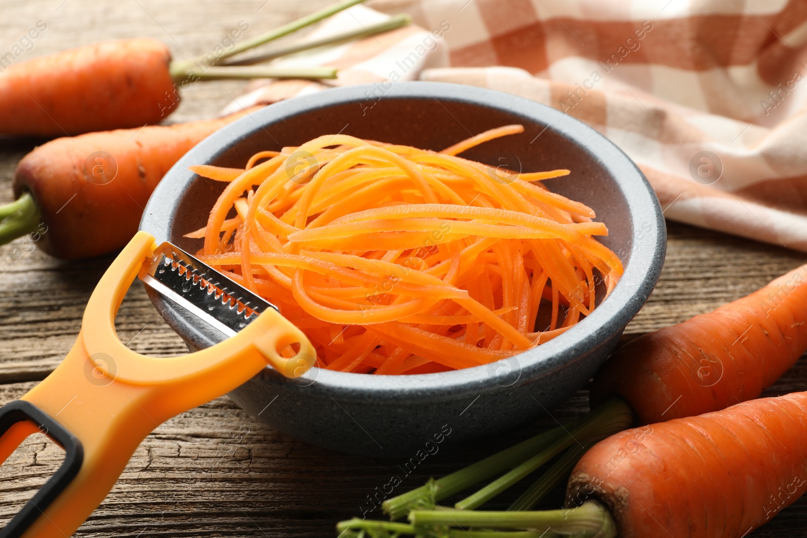 Photo of Raw beetroot noodles, fresh vegetables and peeler on wooden table, closeup. Vegetarian dish