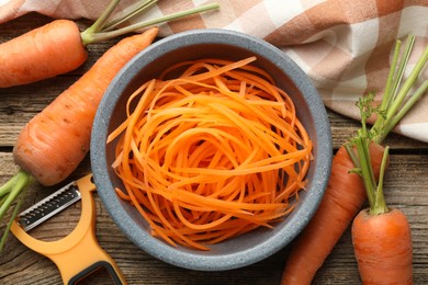 Photo of Raw beetroot noodles, fresh vegetables and peeler on wooden table, flat lay. Vegetarian dish