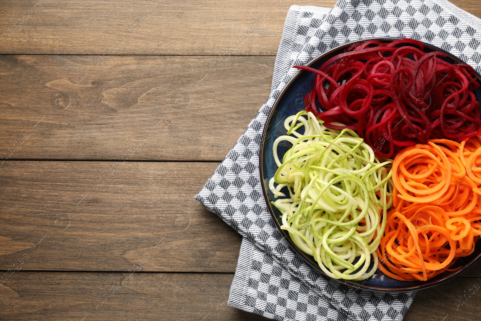 Photo of Vegetarian dish. Different vegetable noodles on wooden table, top view. Space for text