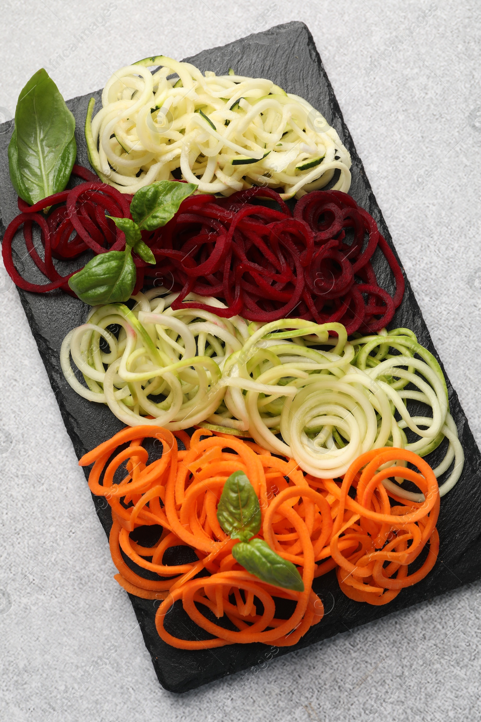Photo of Different vegetable noodles with basil on grey table, top view. Vegetarian dish