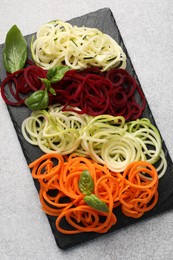 Photo of Different vegetable noodles with basil on grey table, top view. Vegetarian dish