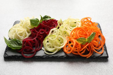 Photo of Different vegetable noodles with basil on grey table, closeup. Vegetarian dish
