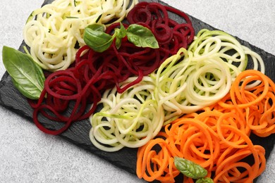 Photo of Different vegetable noodles with basil on grey table, top view. Vegetarian dish