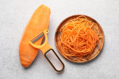 Photo of Vegetable noodles, sweet potato and peeler on light table, flat lay