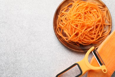 Photo of Vegetable noodles, sweet potato and peeler on light table, flat lay. Space for text