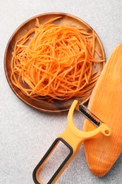 Photo of Vegetable noodles, sweet potato and peeler on light table, flat lay