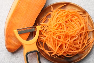 Photo of Vegetable noodles, sweet potato and peeler on light table, flat lay