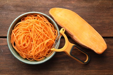 Photo of Vegetable noodles, sweet potato and peeler on wooden table, flat lay
