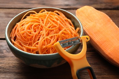 Photo of Vegetable noodles, sweet potato and peeler on wooden table, closeup