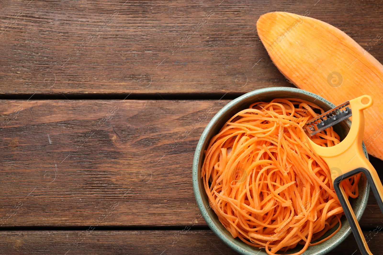 Photo of Vegetable noodles, sweet potato and peeler on wooden table, flat lay. Space for text