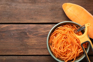 Photo of Vegetable noodles, sweet potato and peeler on wooden table, flat lay. Space for text