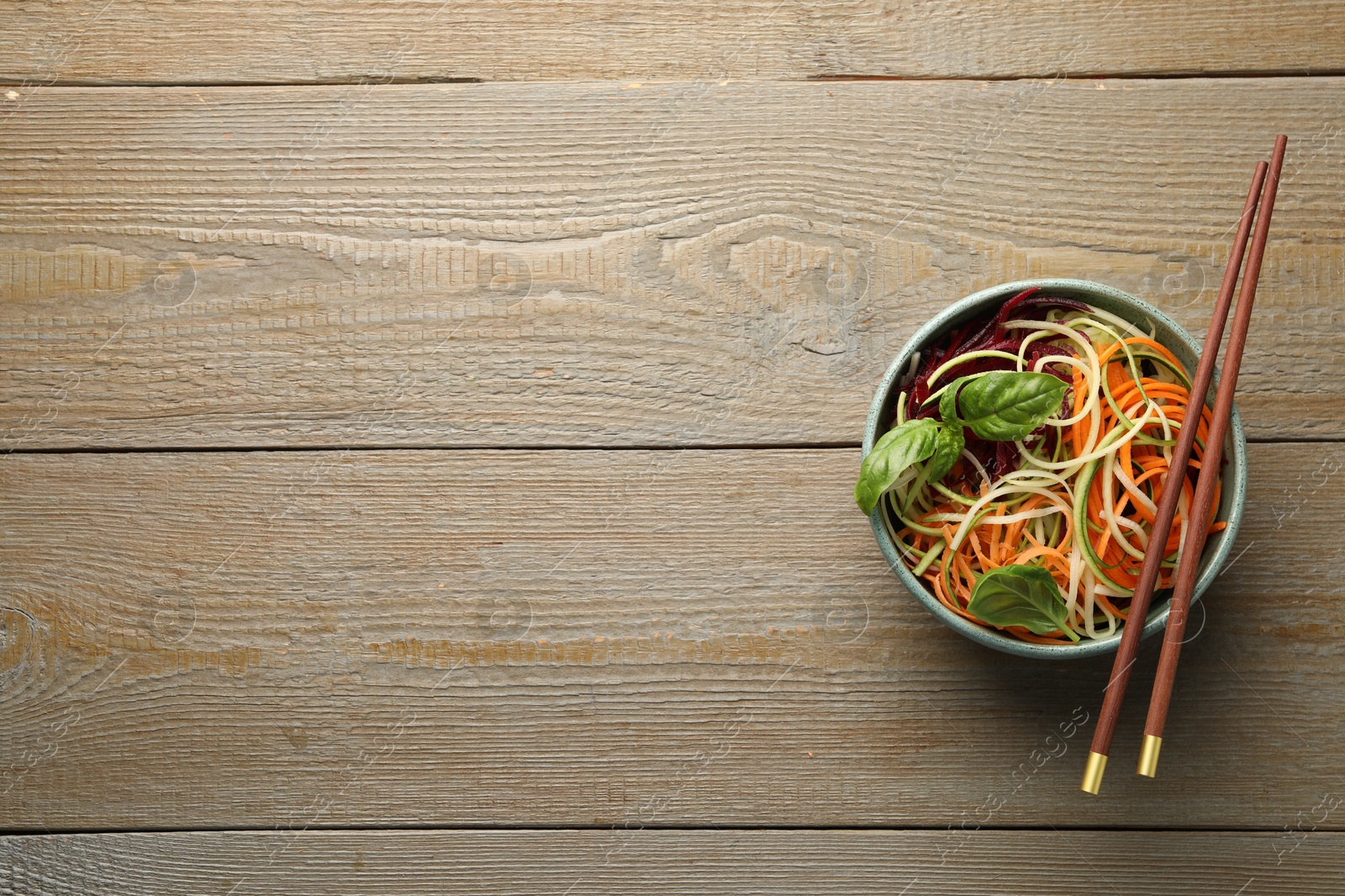 Photo of Tasty vegetable noodles served on wooden table, top view. Space for text