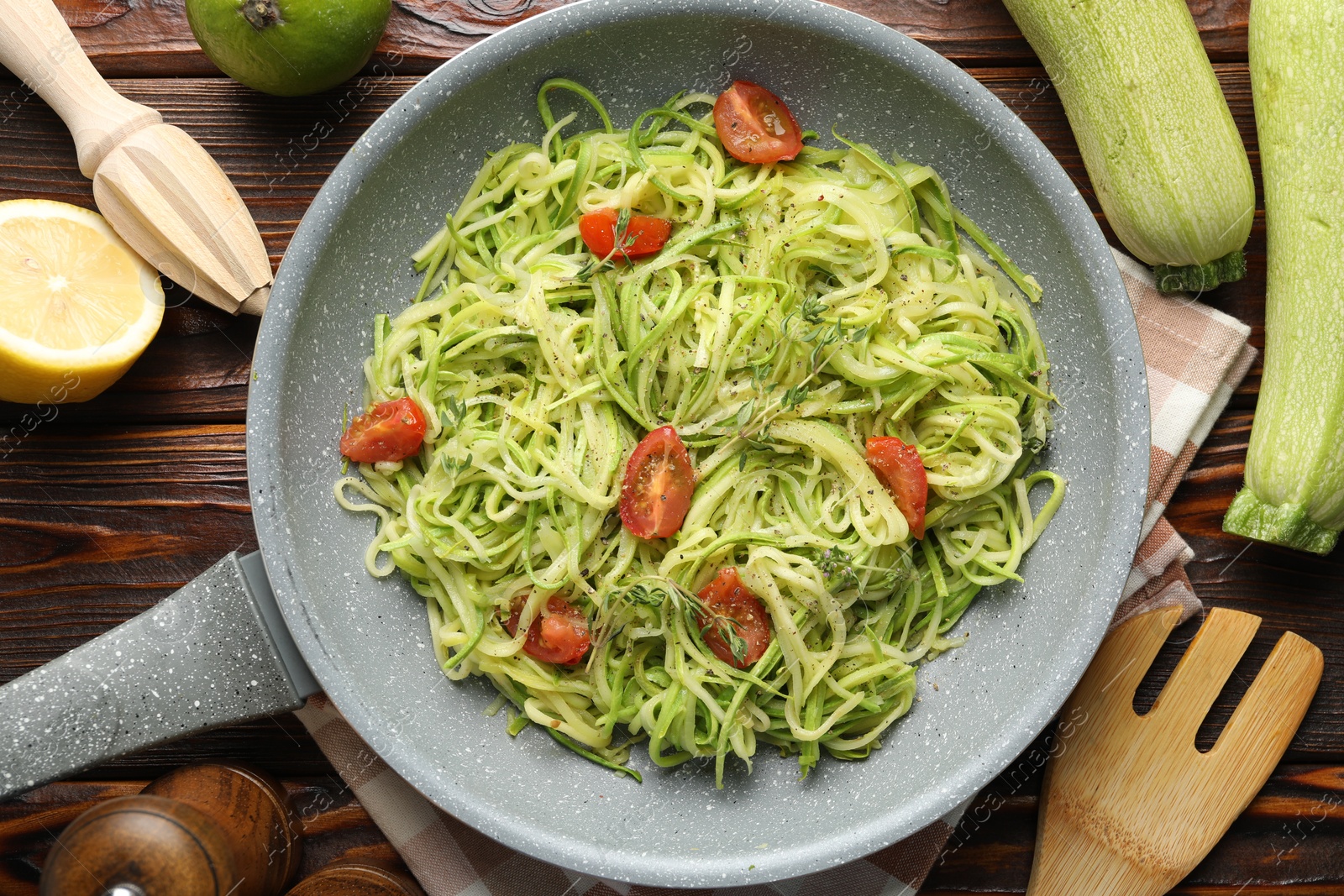 Photo of Tasty zucchini noodles with tomatoes, thyme and ingredients on wooden table, flat lay