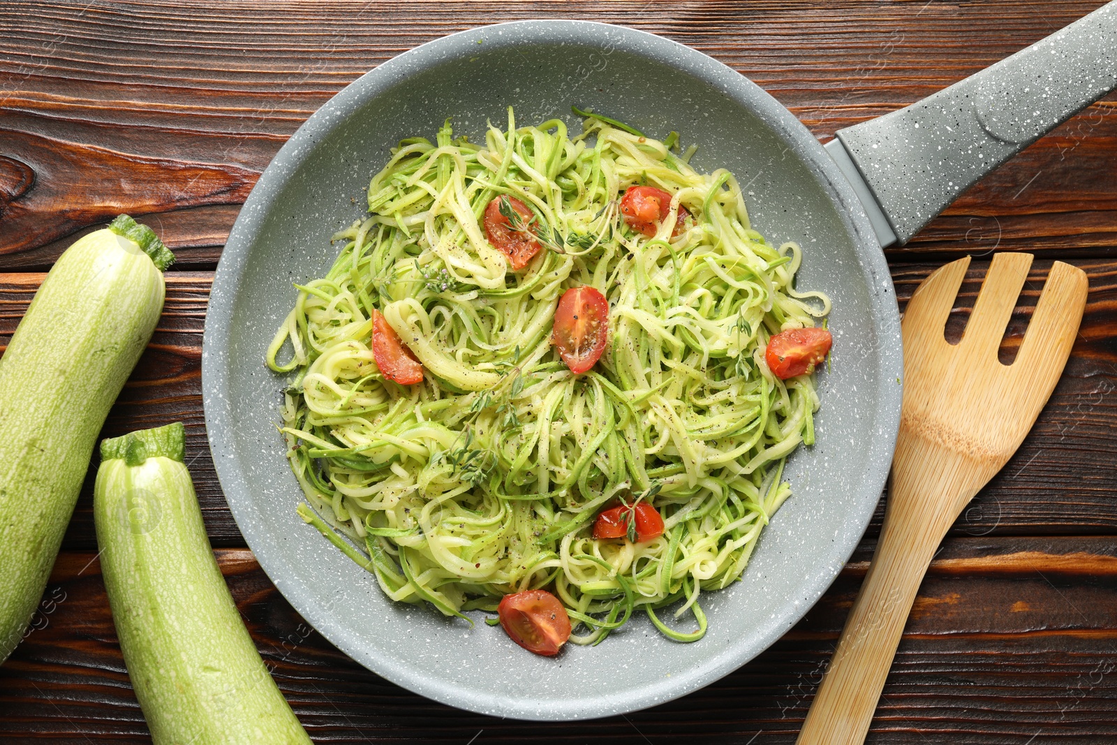 Photo of Tasty zucchini noodles with tomatoes and thyme on wooden table, flat lay