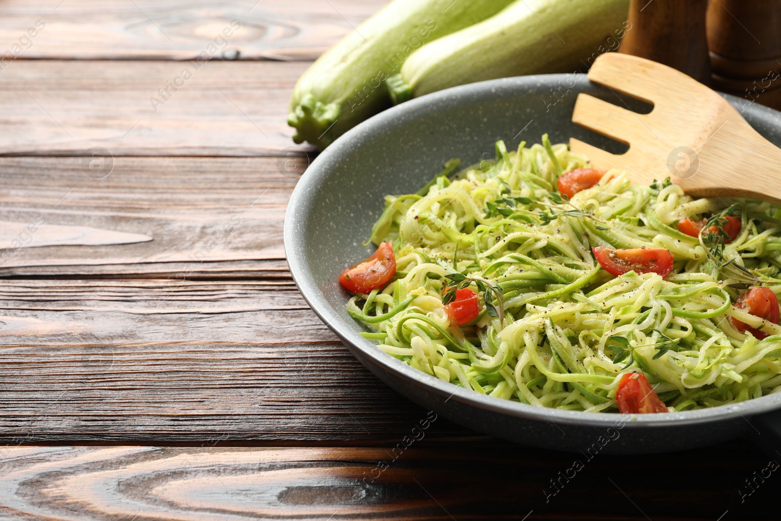 Tasty zucchini noodles with tomatoes and thyme on wooden table, closeup. Space for text Photo of Tasty zucchini noodles with tomatoes and thyme on wooden table, closeup. Space for text