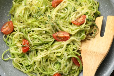 Photo of Tasty zucchini noodles with tomatoes, thyme and turner on frying pan, closeup