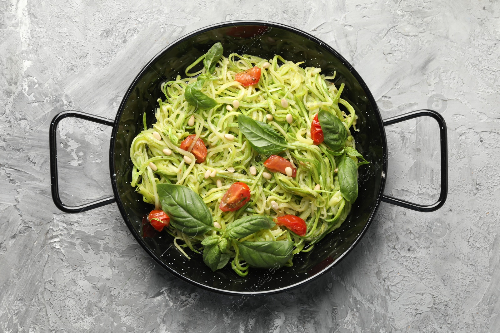 Photo of Tasty zucchini noodles with tomatoes, pine nuts and basil on grey table, top view