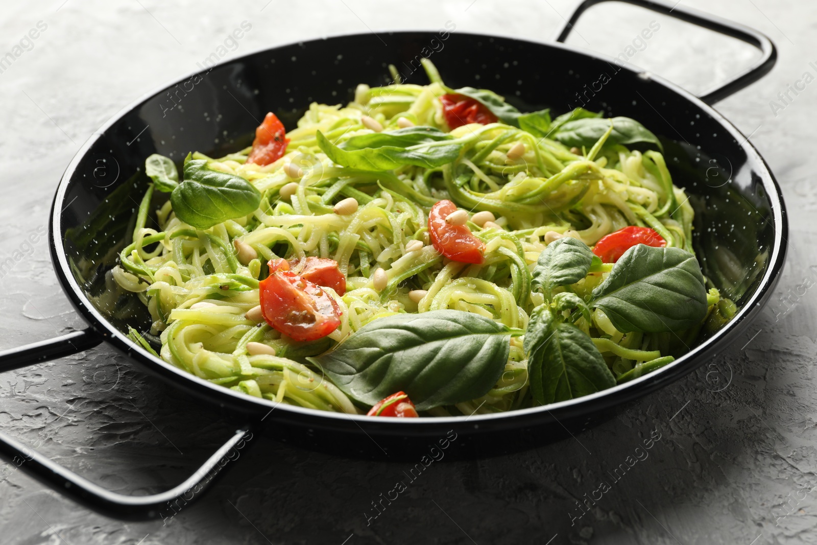 Tasty zucchini noodles with tomatoes, pine nuts and basil on grey table, closeup Photo of Tasty zucchini noodles with tomatoes, pine nuts and basil on grey table, closeup