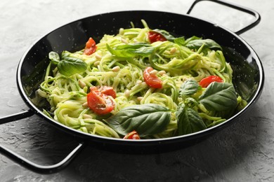 Photo of Tasty zucchini noodles with tomatoes, pine nuts and basil on grey table, closeup