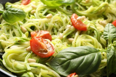 Photo of Tasty zucchini noodles with tomatoes, pine nuts and basil, closeup