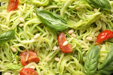 Photo of Tasty zucchini noodles with tomatoes, pine nuts and basil, closeup