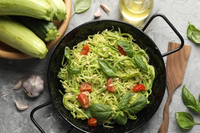 Photo of Tasty zucchini noodles with tomatoes, pine nuts, basil and ingredients on grey table, flat lay