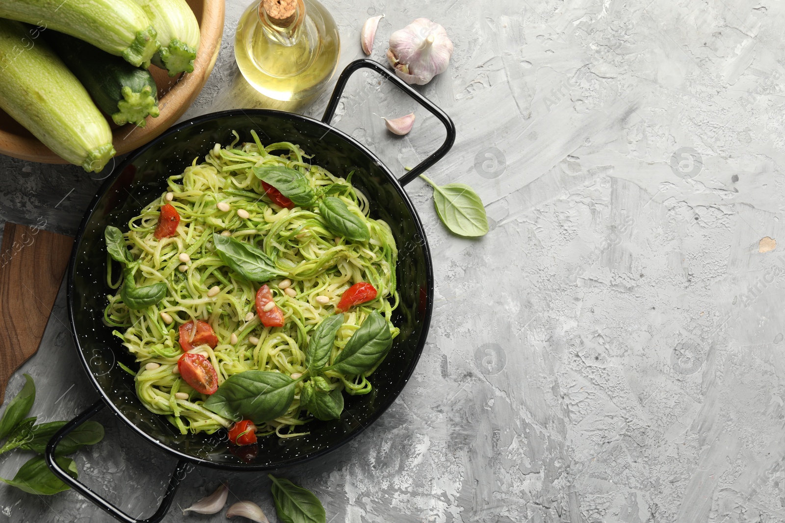 Tasty zucchini noodles with tomatoes, pine nuts, basil and ingredients on grey table, flat lay. Space for text Photo of Tasty zucchini noodles with tomatoes, pine nuts, basil and ingredients on grey table, flat lay. Space for text