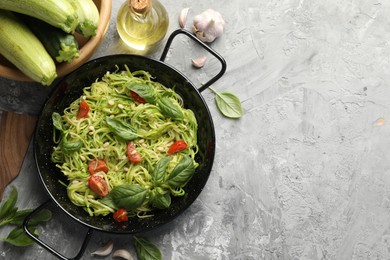 Photo of Tasty zucchini noodles with tomatoes, pine nuts, basil and ingredients on grey table, flat lay. Space for text