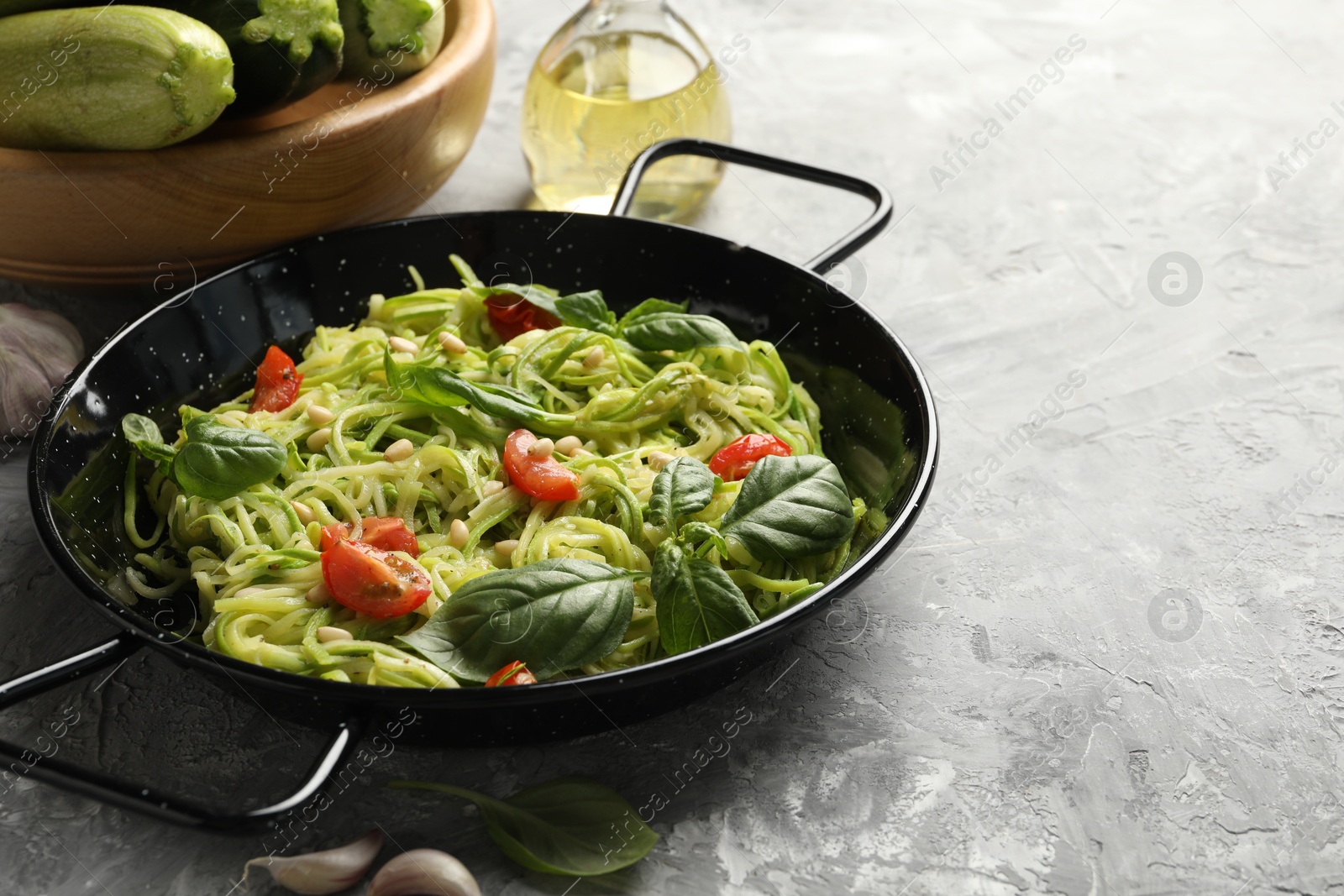 Tasty zucchini noodles with tomatoes, pine nuts, basil and ingredients on grey table, closeup Photo of Tasty zucchini noodles with tomatoes, pine nuts, basil and ingredients on grey table, closeup