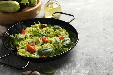 Photo of Tasty zucchini noodles with tomatoes, pine nuts, basil and ingredients on grey table, closeup