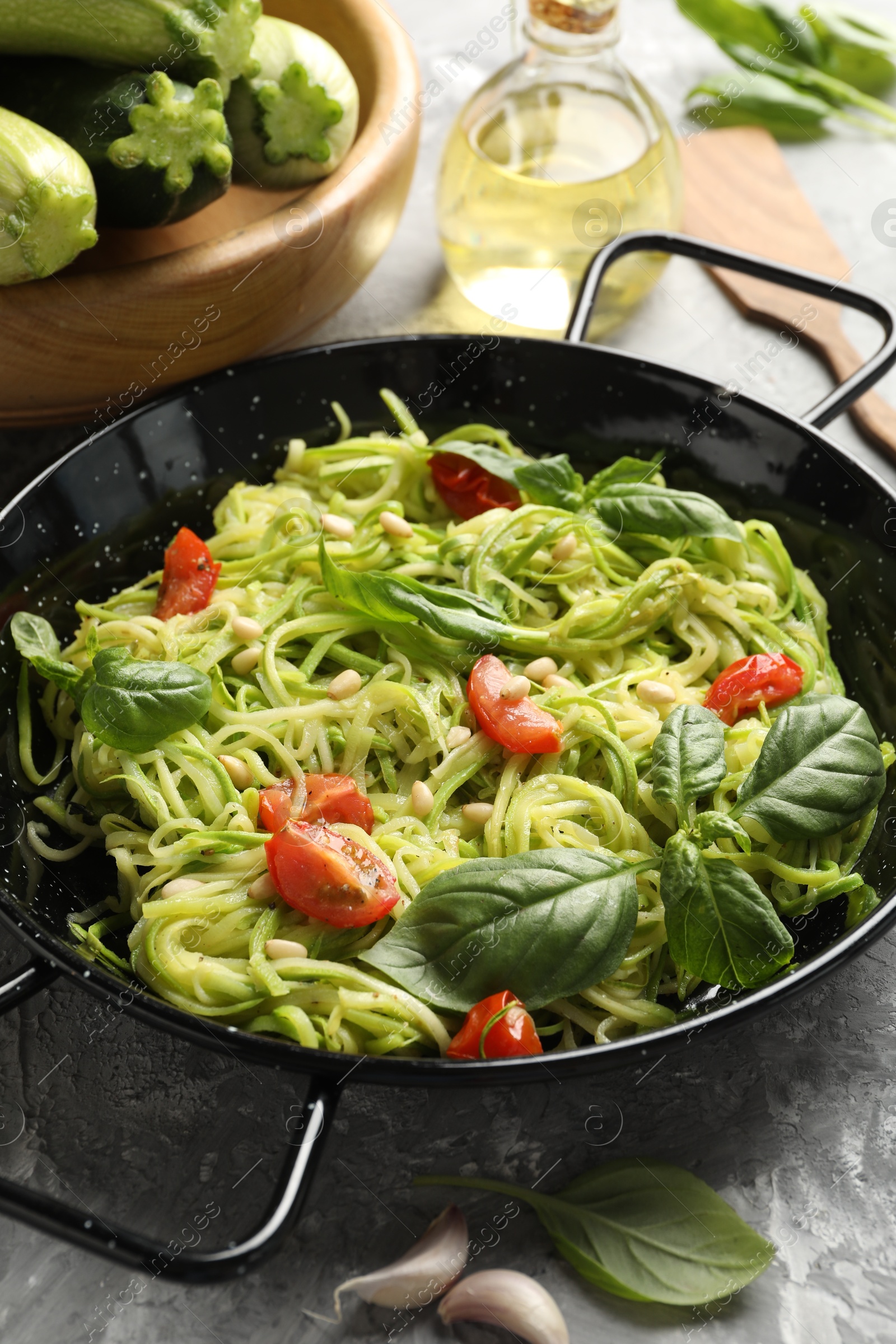 Tasty zucchini noodles with tomatoes, pine nuts, basil and ingredients on grey table, closeup Photo of Tasty zucchini noodles with tomatoes, pine nuts, basil and ingredients on grey table, closeup