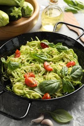 Photo of Tasty zucchini noodles with tomatoes, pine nuts, basil and ingredients on grey table, closeup