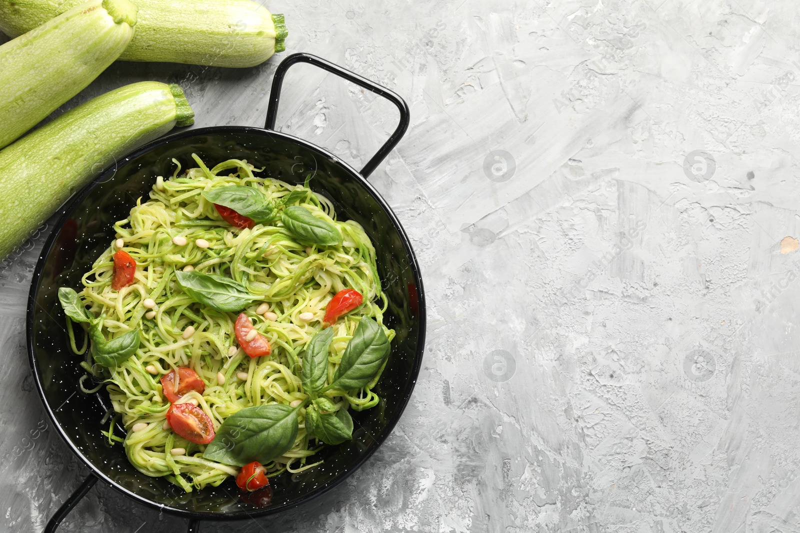 Photo of Tasty zucchini noodles with tomatoes, pine nuts, basil and ingredients on grey table, flat lay. Space for text