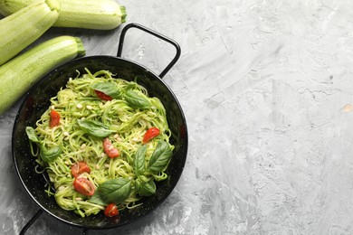 Photo of Tasty zucchini noodles with tomatoes, pine nuts, basil and ingredients on grey table, flat lay. Space for text