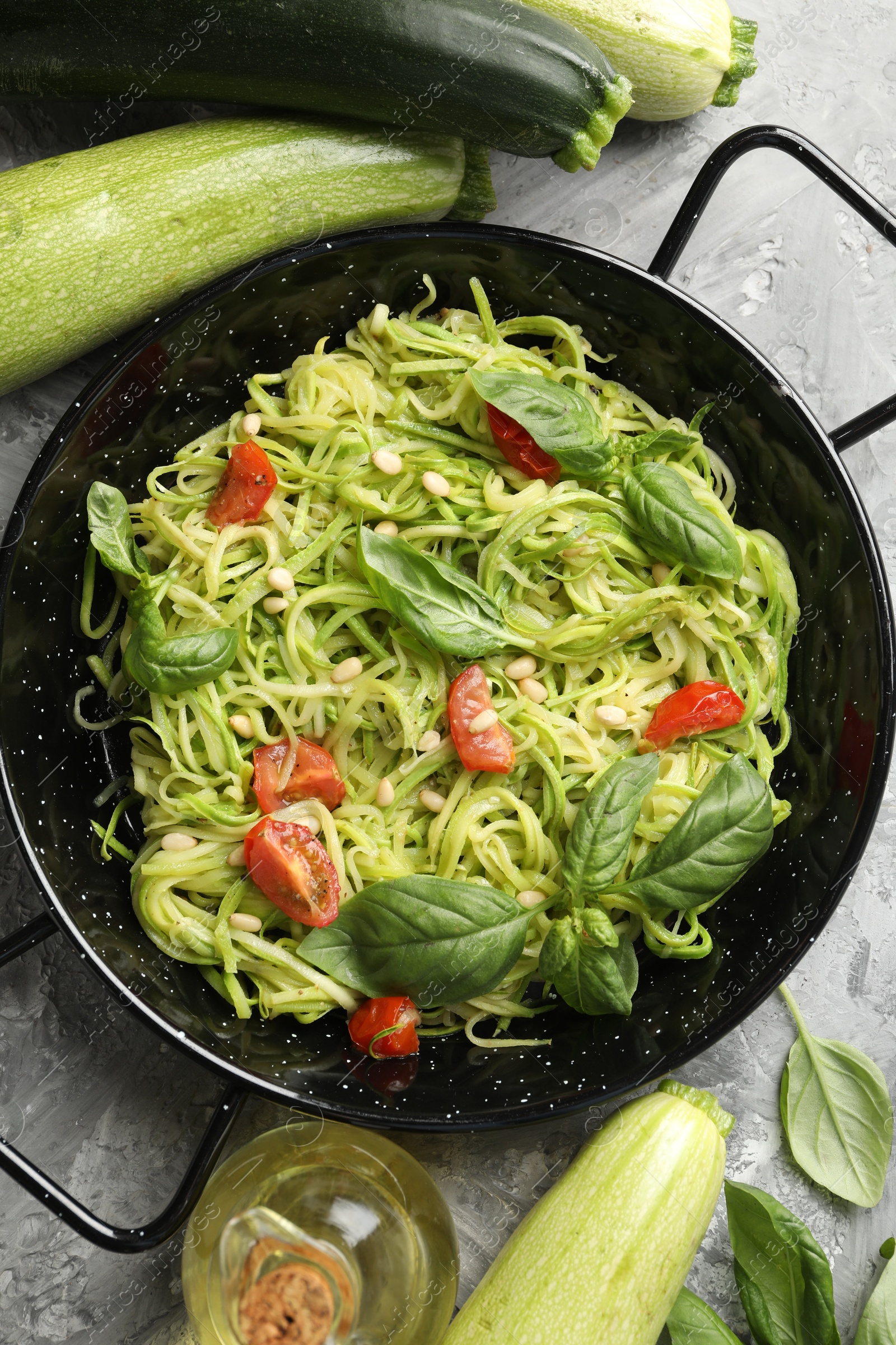 Tasty zucchini noodles with tomatoes, pine nuts, basil and ingredients on grey table, flat lay Photo of Tasty zucchini noodles with tomatoes, pine nuts, basil and ingredients on grey table, flat lay