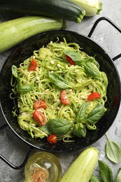 Photo of Tasty zucchini noodles with tomatoes, pine nuts, basil and ingredients on grey table, flat lay