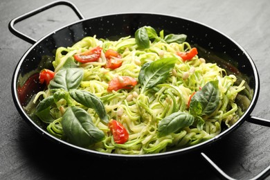 Photo of Tasty zucchini noodles with tomatoes, pine nuts and basil on black table, closeup