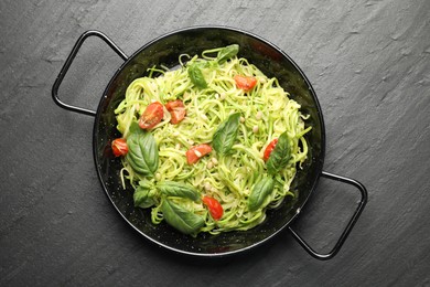 Photo of Tasty zucchini noodles with tomatoes, pine nuts and basil on black table, top view