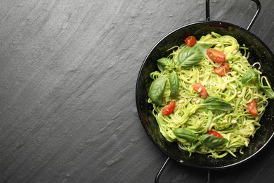 Photo of Tasty zucchini noodles with tomatoes, pine nuts and basil on black table, top view. Space for text