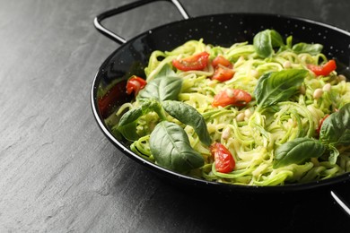 Photo of Tasty zucchini noodles with tomatoes, pine nuts and basil on black table, closeup