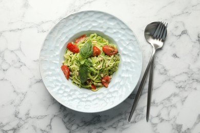 Photo of Tasty zucchini noodles with tomatoes, pine nuts and basil served on white marble table, top view