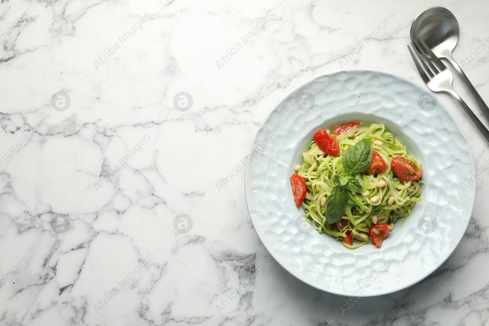 Photo of Tasty zucchini noodles with tomatoes, pine nuts and basil served on white marble table, top view. Space for text