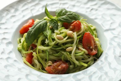 Photo of Tasty zucchini noodles with tomatoes, pine nuts and basil, closeup
