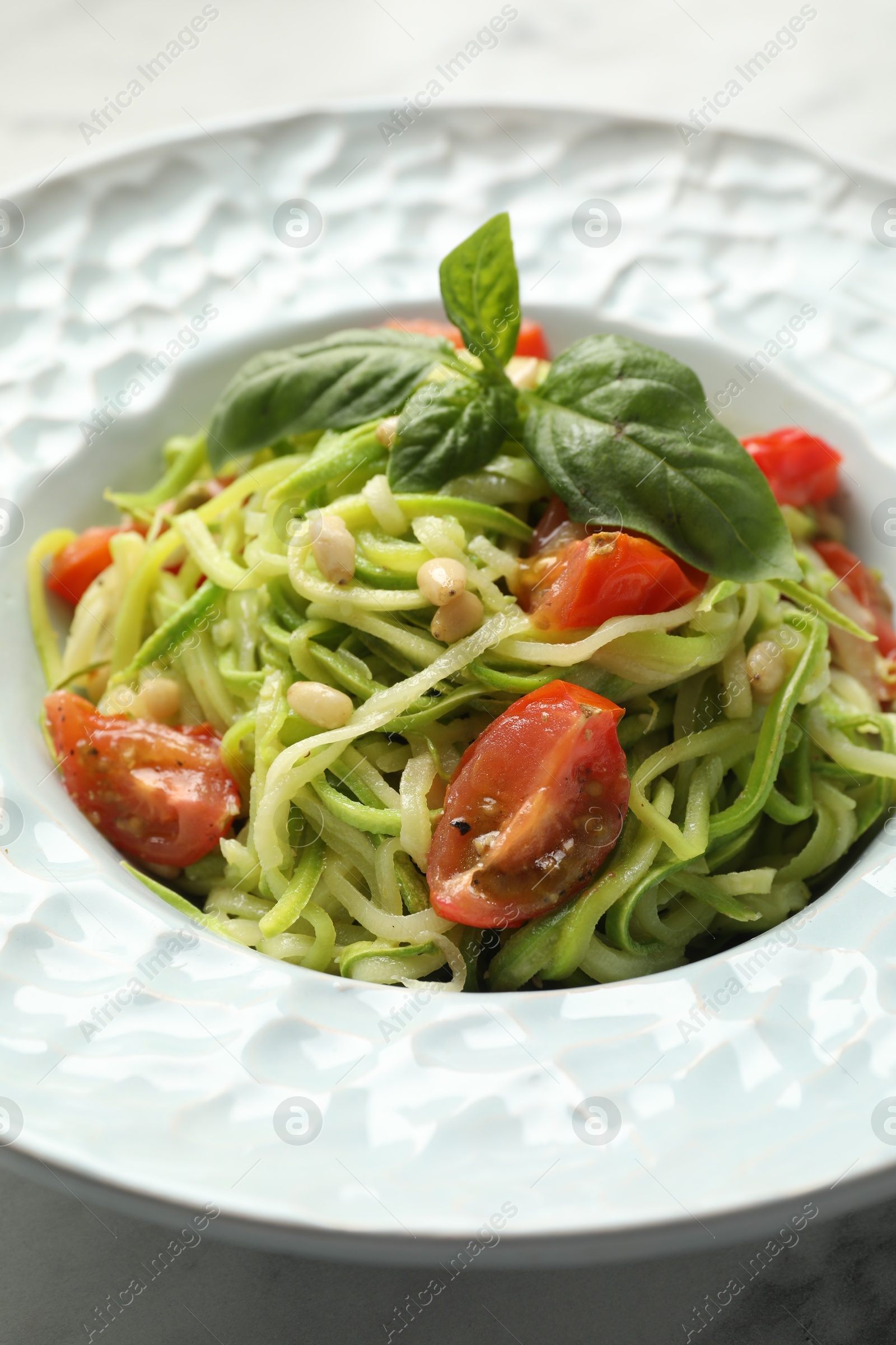 Photo of Tasty zucchini noodles with tomatoes, pine nuts and basil on white table, closeup