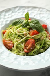 Photo of Tasty zucchini noodles with tomatoes, pine nuts and basil on white table, closeup