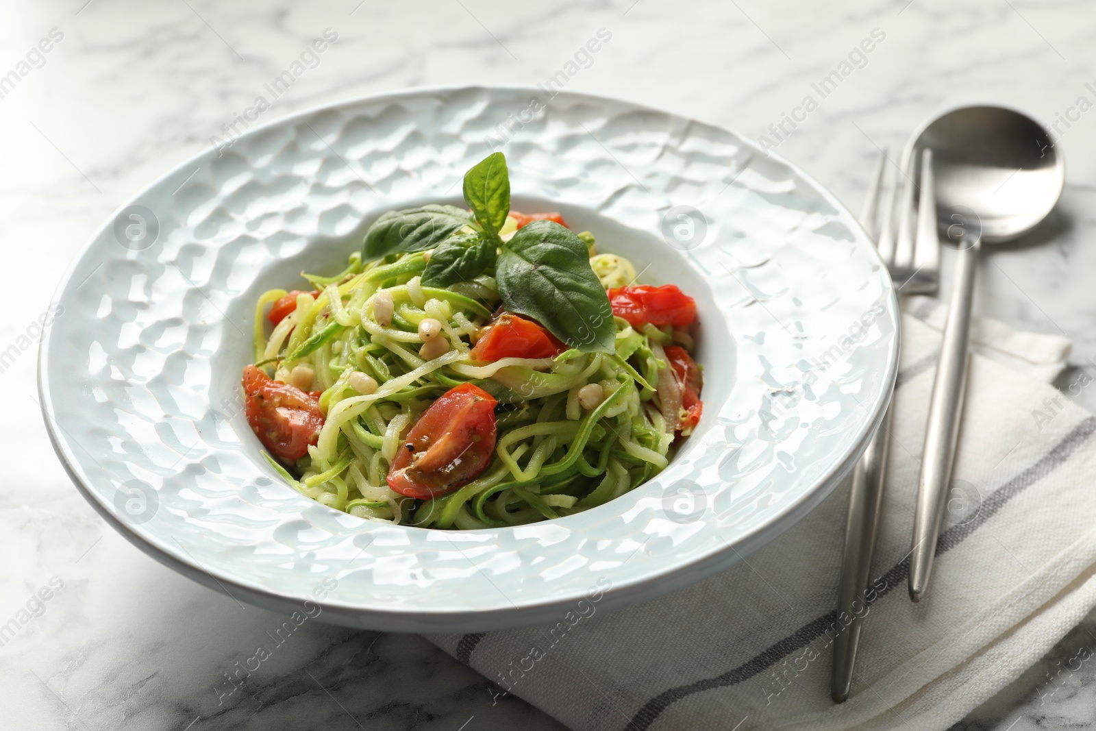 Tasty zucchini noodles with tomatoes, pine nuts and basil served on white marble table, closeup Photo of Tasty zucchini noodles with tomatoes, pine nuts and basil served on white marble table, closeup